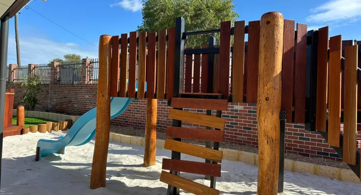 Timber play structure with slide and soft sand base, part of the natural outdoor play area at Amara Balga.