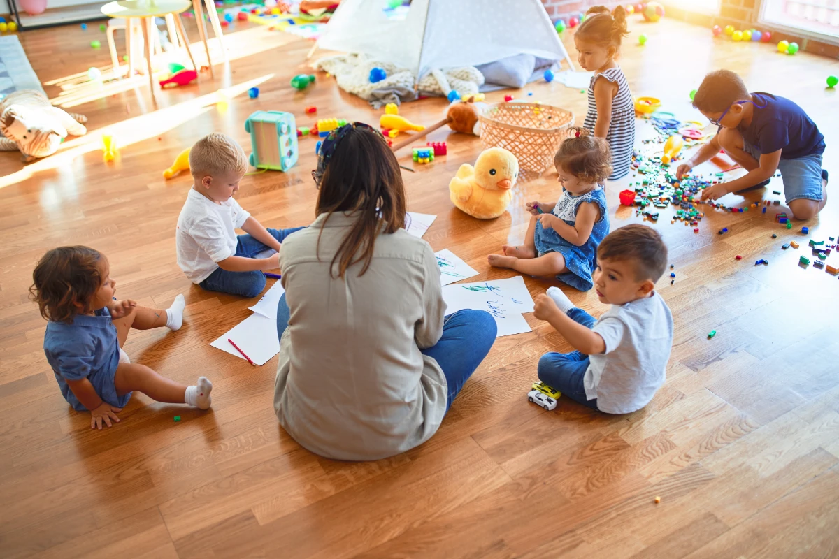 Toddlers sitting in a group with an educator, drawing and exploring creative activities together