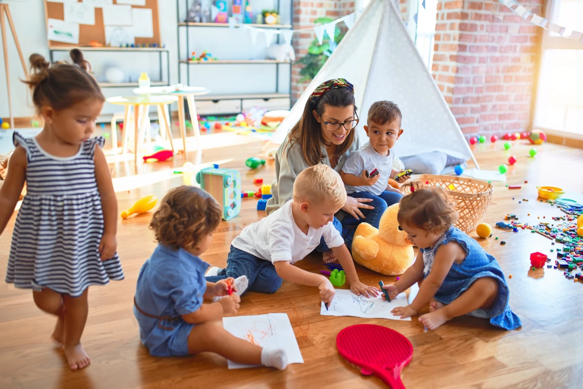 Group of toddlers drawing and playing together with an educator, exploring creativity and connection
