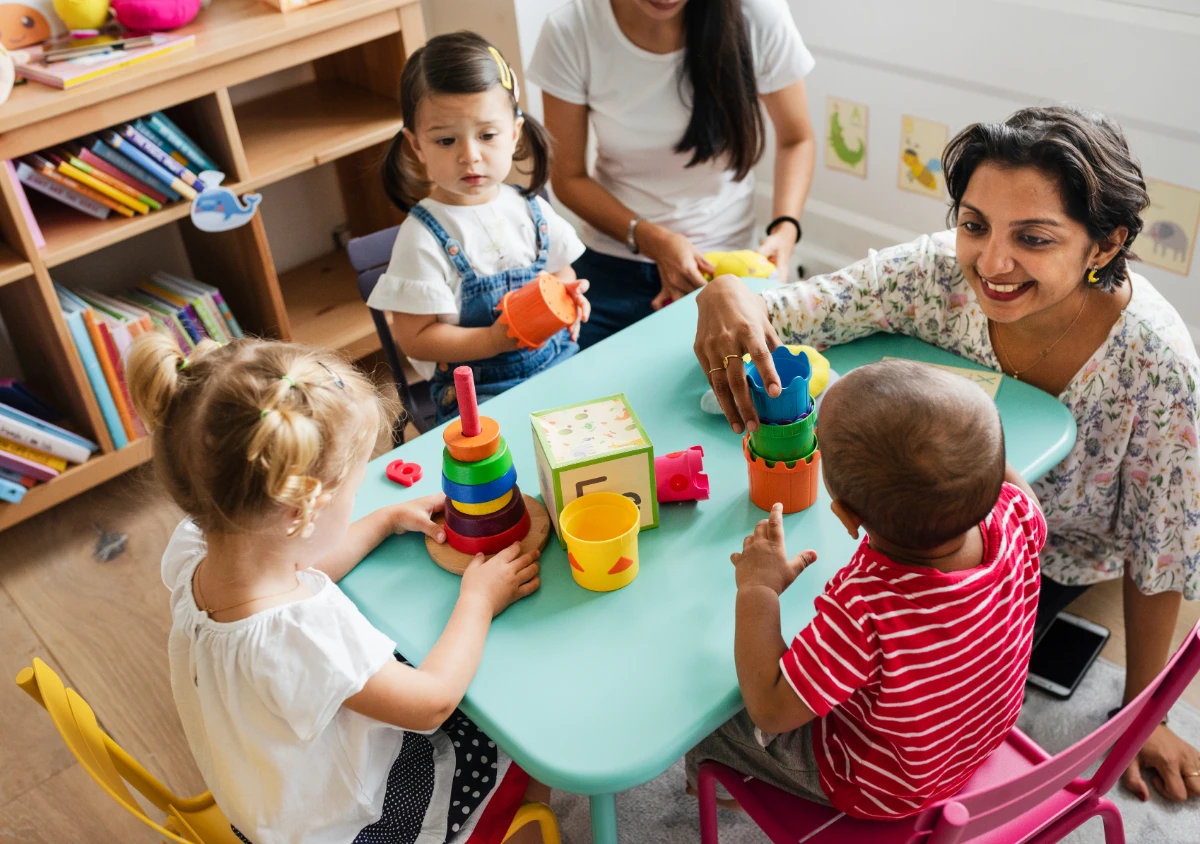 Toddlers exploring shapes, sizes and stacking toys with educators supporting their learning