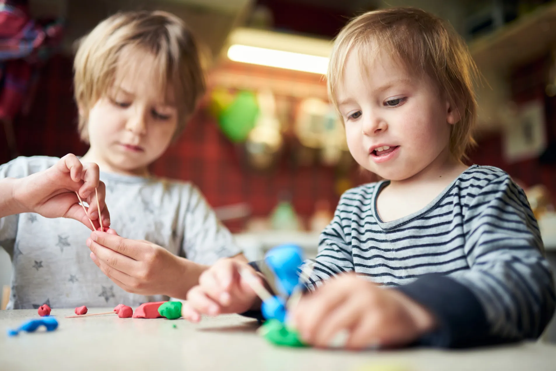 Two young children playing with colourful modelling clay, one shaping pieces with toothpicks and the other working on a creation.