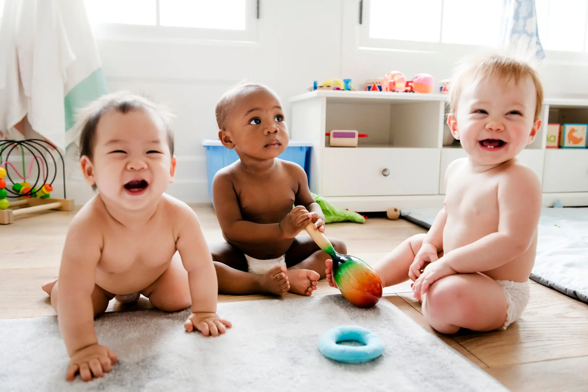 Three babies playing on the floor with musical instruments in a safe, stimulating environment designed for exploration and discovery.