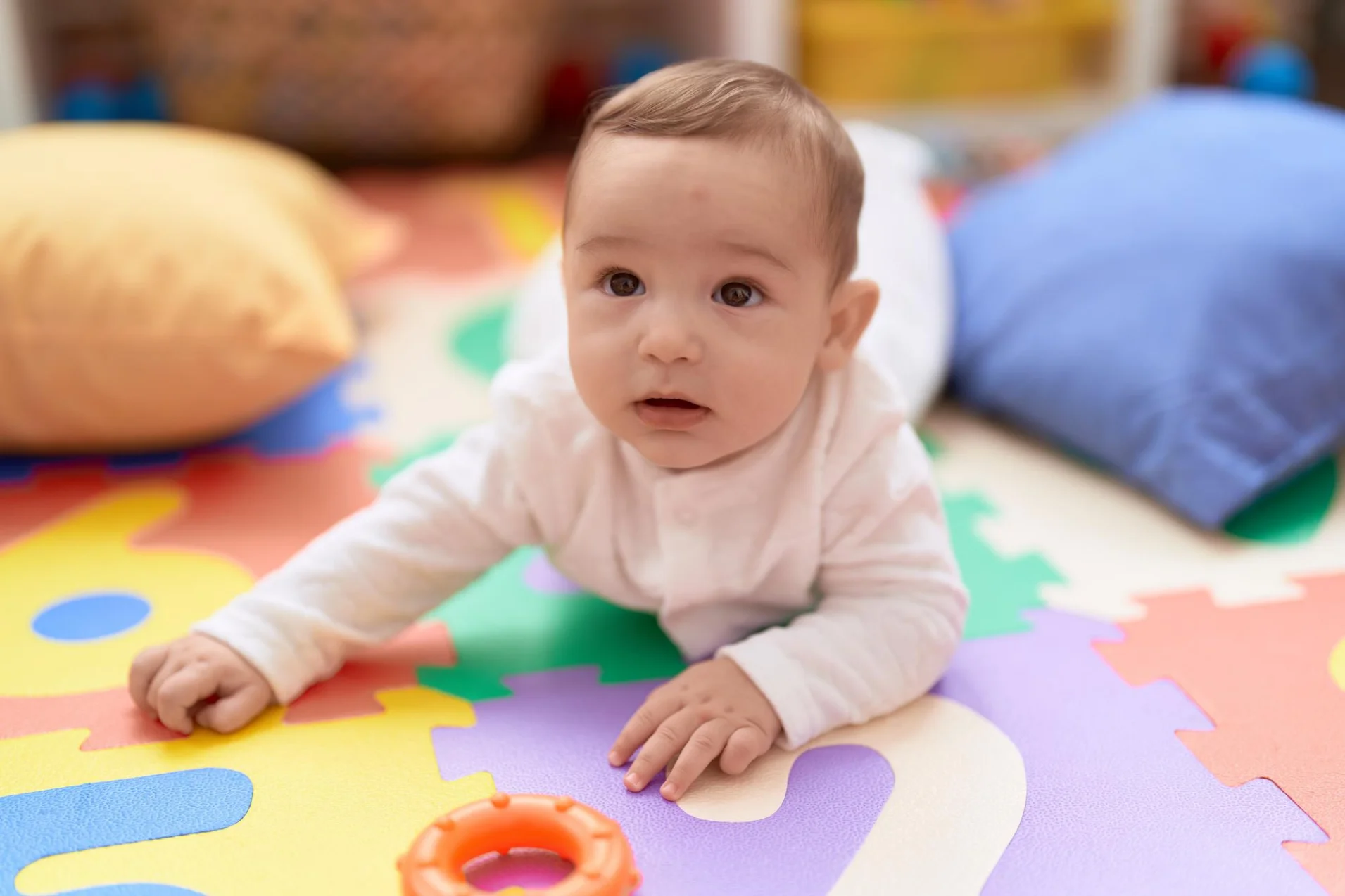 A baby crawling on soft play mats, surrounded by colourful toys, in a nurturing and calm early learning space.