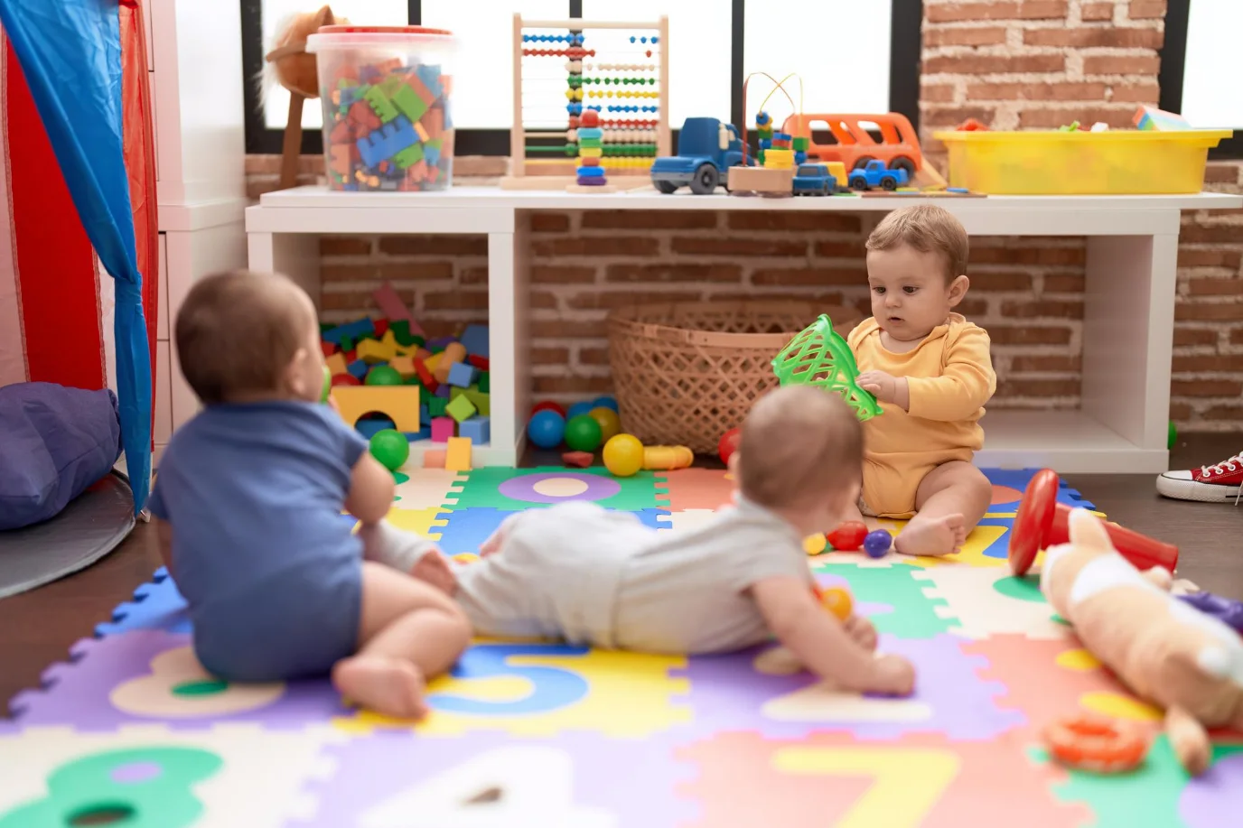 Infants playing with colourful stacking toys on soft mats in a bright and supportive learning environment.