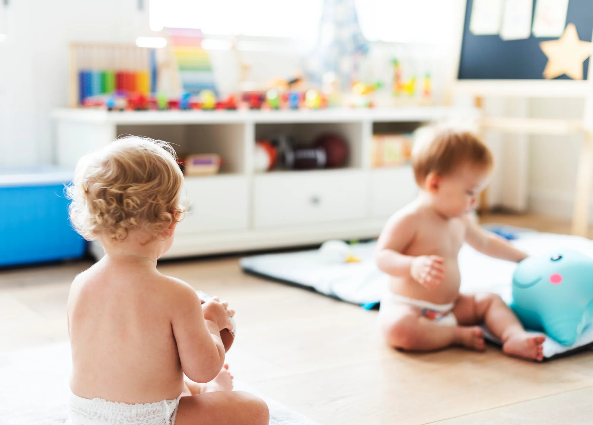 A baby sitting on the floor, playing with colourful blocks, in a space filled with soft furnishings for comfort.