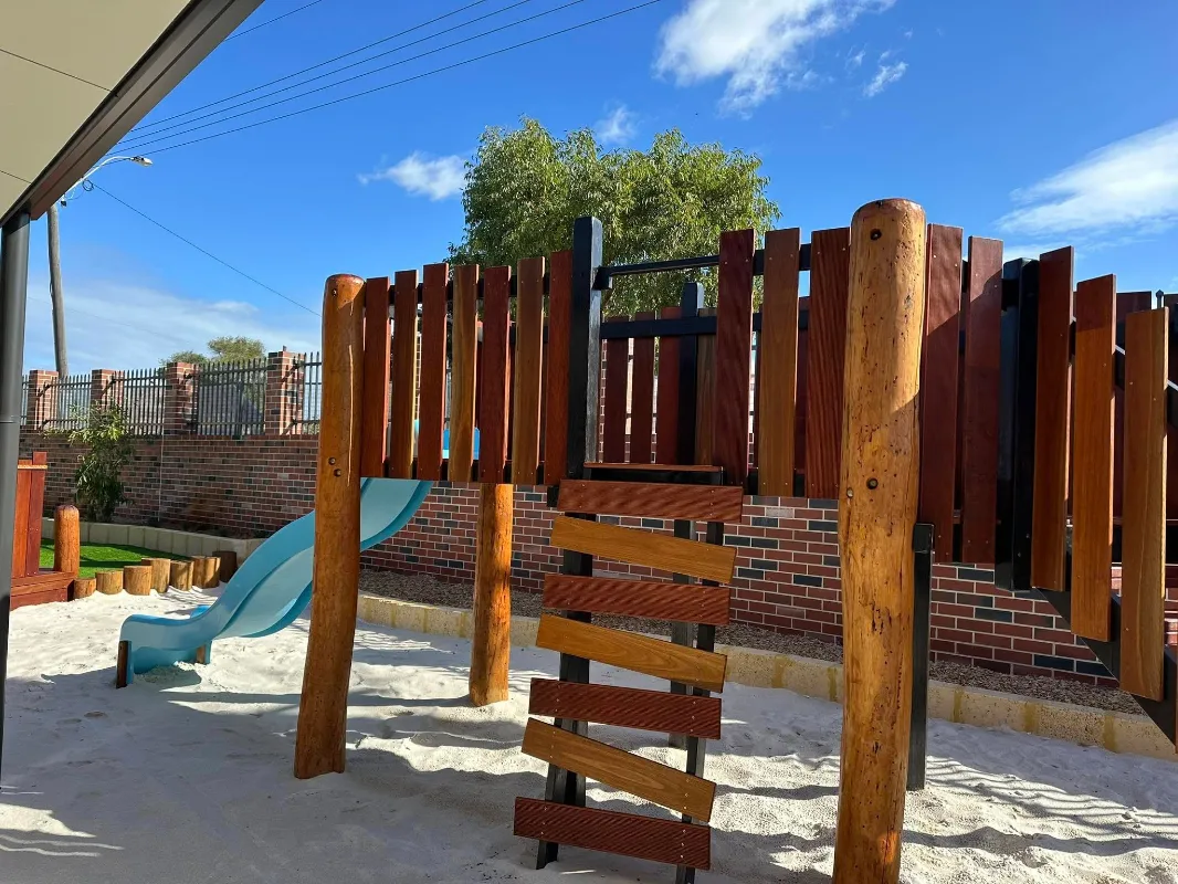 Timber play structure with slide and soft sand base, part of the natural outdoor play area at Amara Balga.