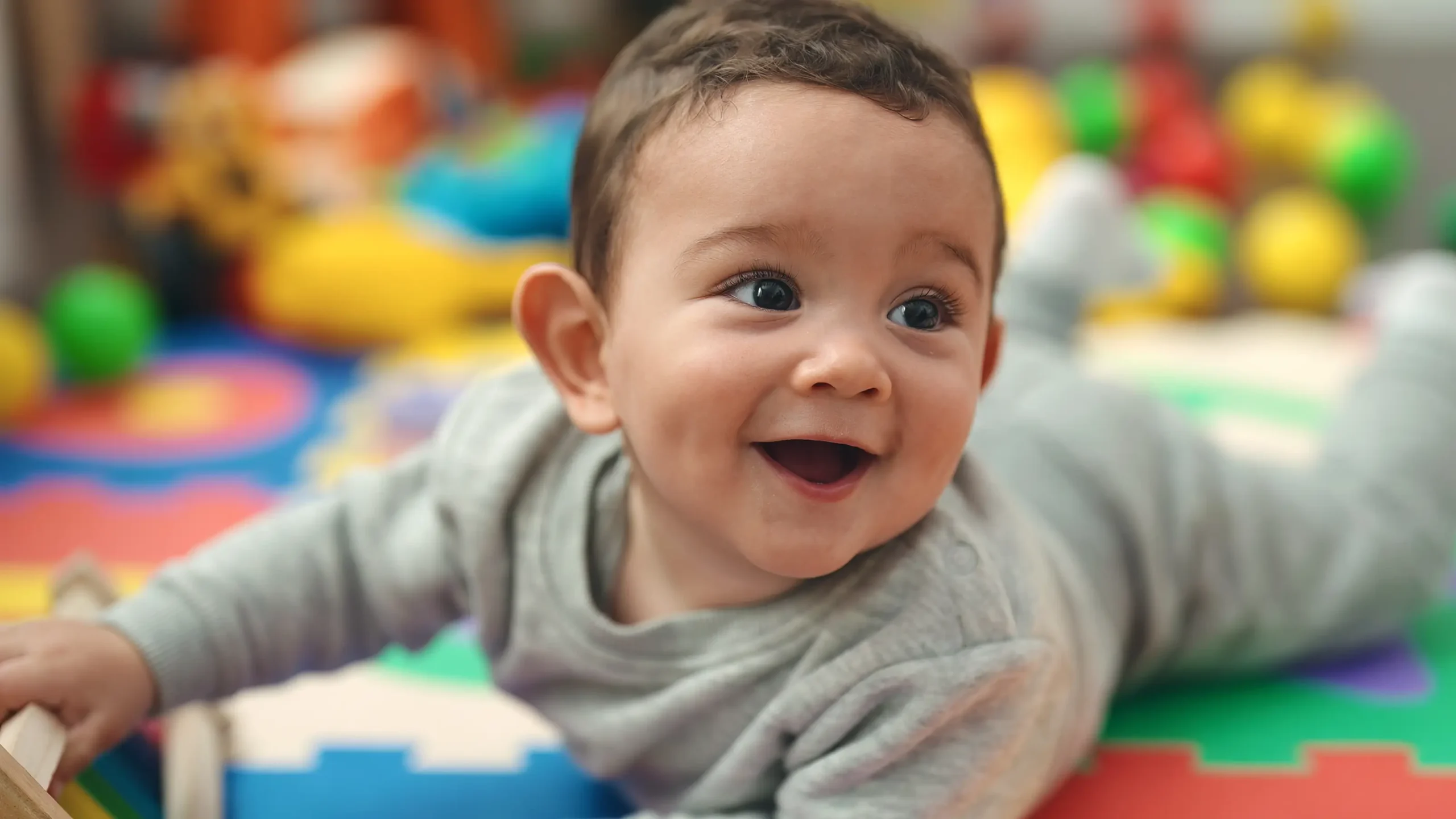 A baby crawling on a colourful playmat with bright, oversized building blocks in a vibrant, playful setting.