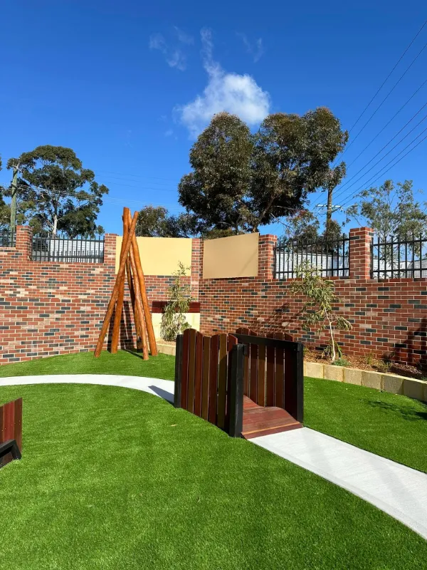 Landscaped outdoor space with soft artificial grass, wooden tunnels, and natural log structures for creative exploration.