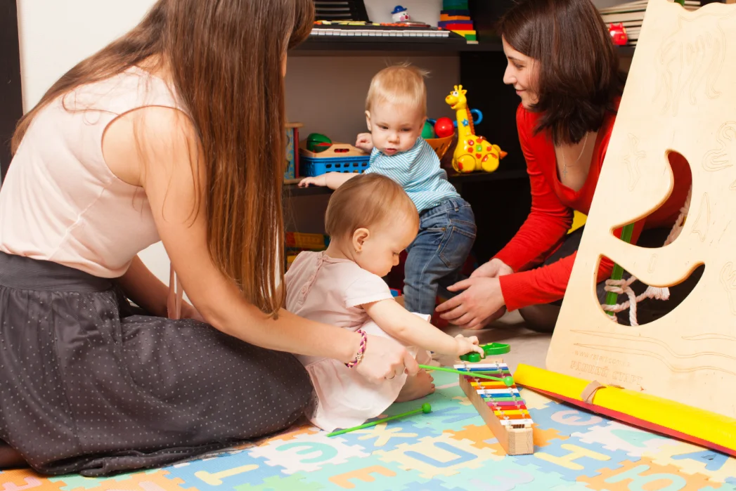 Two educators engaging with babies during playtime, helping them interact with colourful toys in a nurturing space.