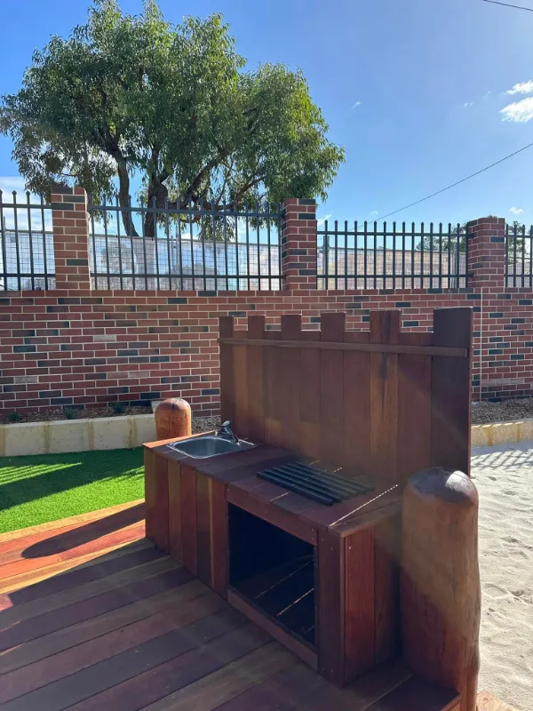 Outdoor mud kitchen made from timber with a play sink and stovetop, encouraging imaginative play in a natural setting.