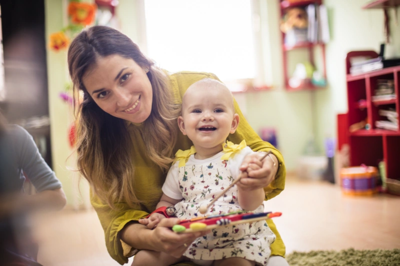 An expert educator and a smiling baby playing with a colourful toy, providing nurturing support for early learning and development.
