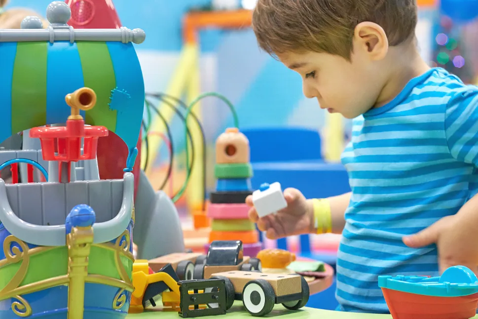 Young boy playing with toy blocks, focused on building with colourful pieces in a playroom.