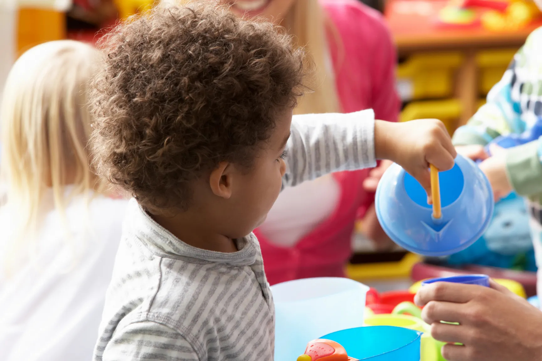 Child engaged in sensory play, using a toy teapot to explore water and fine motor skills.