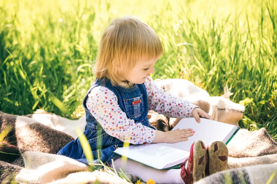 Toddler reading a book outside during quiet outdoor time