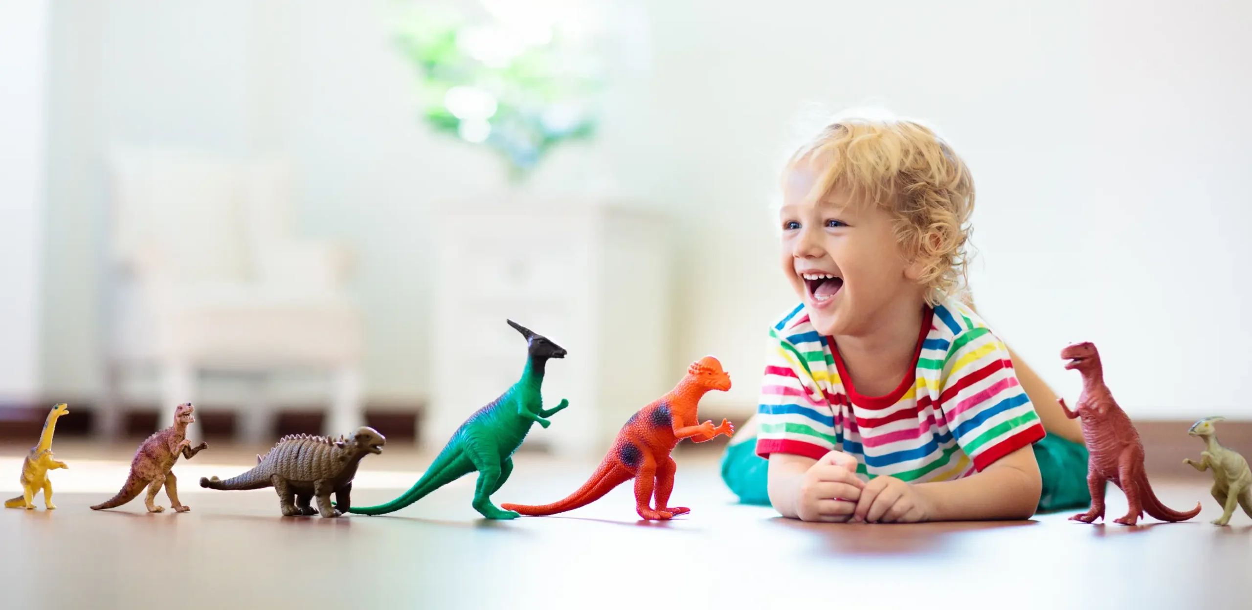 Toddler smiling while playing with dinosaur toys in the Giraffe Room