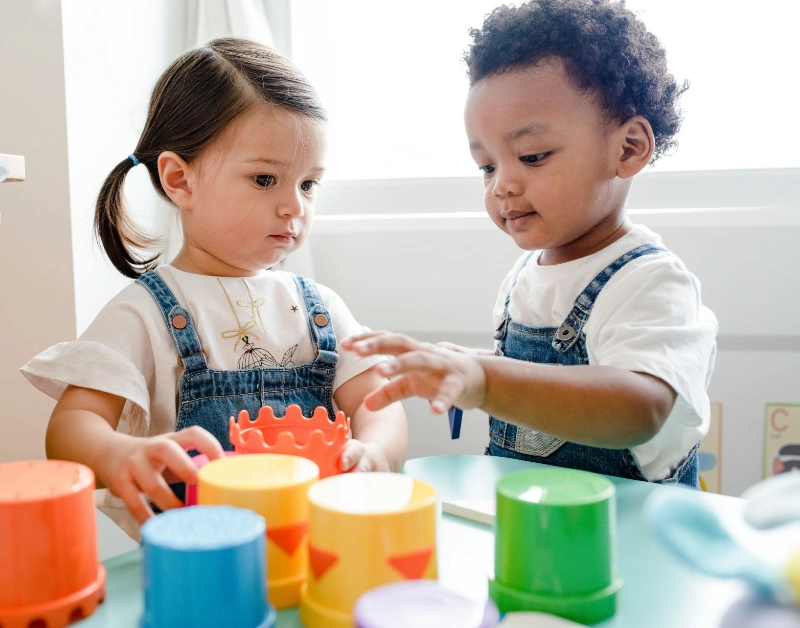 Two toddlers engaging in creative play with colourful toys, developing friendships and social skills