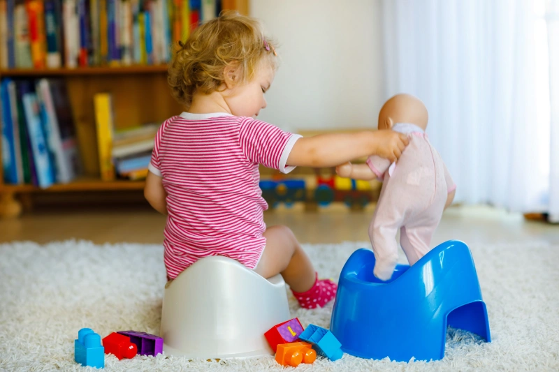 Toddler practising toilet training with a doll, building confidence and independence